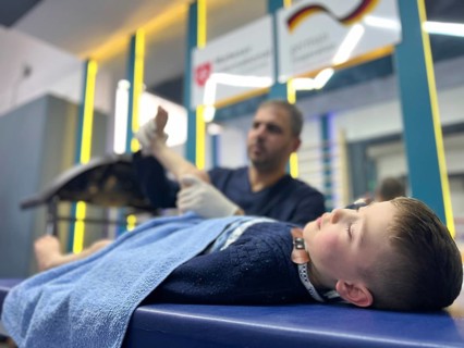 A displaced Syrian child receiving physical therapy from a physiotherapist after a war injury.