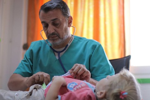 A doctor examining a displaced Syrian child inside a mobile clinic at a refugee camp. Aleppo, Syria