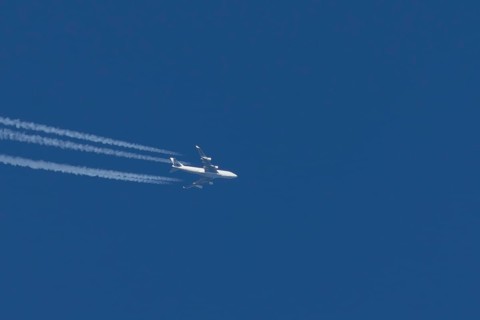 Boeing 747 jumbo jet cargo aircraft with a vapour trail or contrail flying in a blue sky, England,