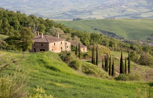 Farmhouse on a gentle hill with cypress trees, surrounded by lush green countryside and sweeping