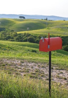 Red standing letterbox in a field with lush green hills in the background, Tuscany, Italy
