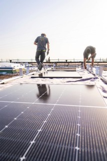 Two workers install solar panels on a sunny roof, PV installation, commercial customers, new build,