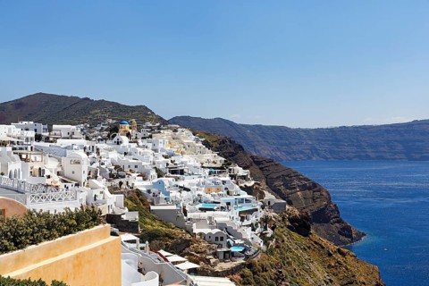 White and colourfully painted holiday homes, orthodox church with blue dome on the edge of the
