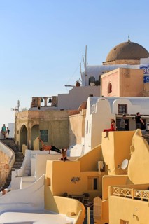 Tourists pose on colourfully painted houses on the hillside, picturesque village of Oia, Thira,