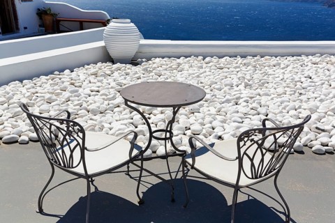 White gravelled area, wrought-iron table and two chairs, vase on a terrace by the sea, Oia,