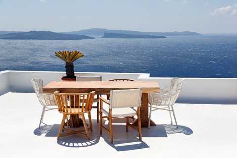 Wooden table and various chairs on a white terrace by the sea, view of the caldera, Oia, Santorini,
