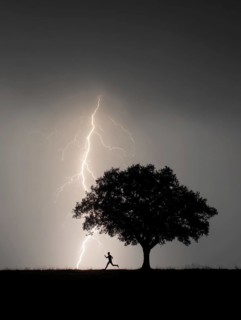 A person runs past a tree in the dark while lightning strikes in the background, danger to life due
