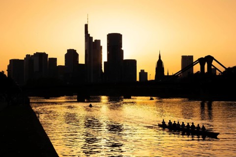 A rowing boat navigates the Main as the sun sets behind the Frankfurt banking skyline, Frankfurt am