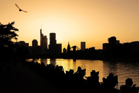 People sitting on the banks of the Main in the evening while the sun sets behind the Frankfurt