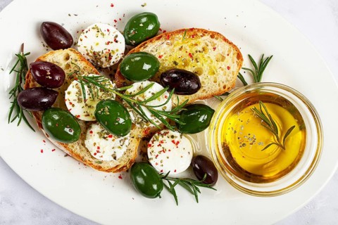 A plate with a snack, ciabatta bread with cheese and olives, olive oil, spices and herbs, top view,