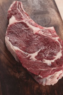 Raw rib eye steak, cowboy steak, wooden chopping board, marble table, top view, no people