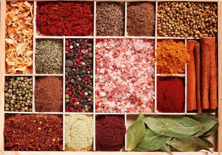An assortment of spices laid out on a wooden tray, arranged in wooden compartments, top view