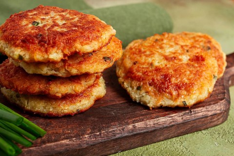 Crispy potato pancakes Latkes, stacked on a wooden board next to fresh green onions, natural light,