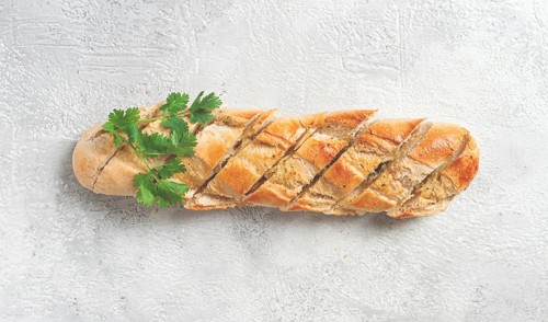 Garlic bread, baguette with garlic butter and herbs, on a light table, top view