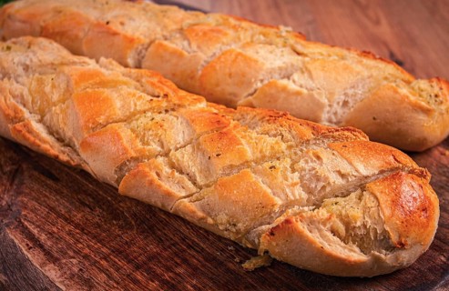 Garlic bread, baguette with garlic butter and herbs, on a wooden board, with herbs and garlic