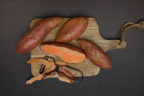 Sweet potatoes with potato peeler on wooden board, Ipomoea batatas