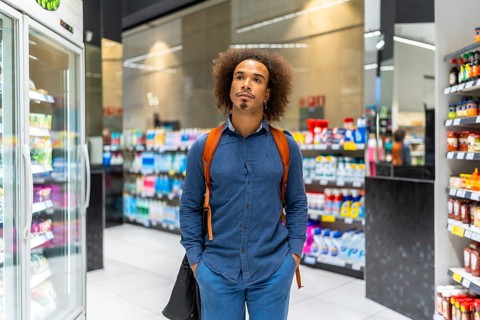Young man with afro hair stands in a supermarket aisle, thoughtfully comparing products and