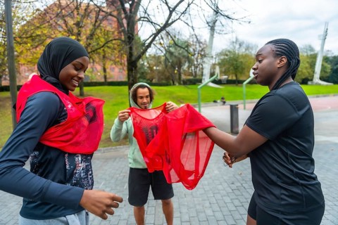 Diverse friends smiling and gearing up on an outdoor urban basketball court, putting on team bibs