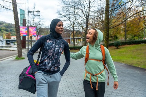 Diverse young adult friends wearing activewear walking and talking in an urban park, sharing a