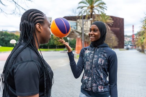 Two diverse young women enjoying a friendly basketball game at an outdoor court, one skillfully