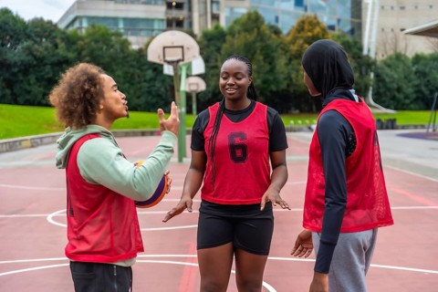 Diverse young adults on an urban basketball court talking strategy and bonding over streetball,