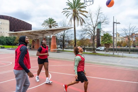 Diverse group of young adult friends playing basketball on an urban court, with a woman wearing a