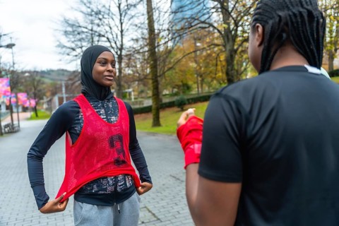Young black woman wearing a hijab and training bib talking with a friend while preparing for her
