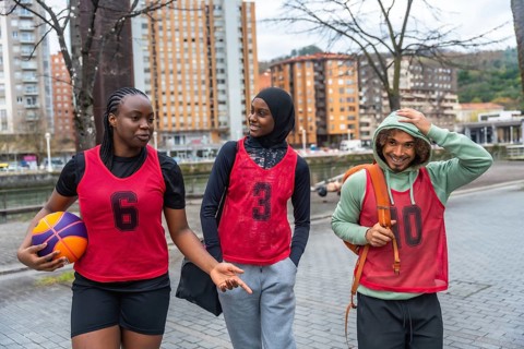 Diverse friends in sportswear and bibs walking and conversing on an urban street, carrying a