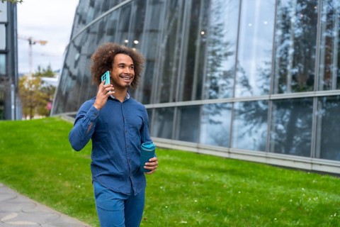 Smiling young Mixed-race man with curly hair walking confidently along a modern office building,