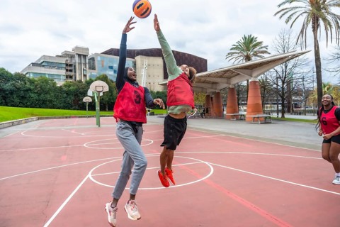 Diverse young women are jumping and reaching for a ball during a friendly outdoor basketball game
