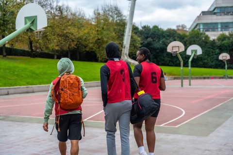 Young diverse friends wearing sports bibs and carrying bags, walking united towards basketball