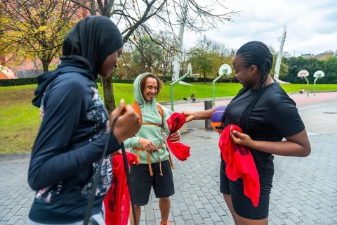 Diverse friends on an urban basketball court smiling and holding red pennants, preparing to play