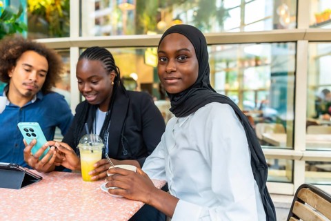 Diverse group of young friends at a cafe laughing and sharing content on a smartphone, enjoying
