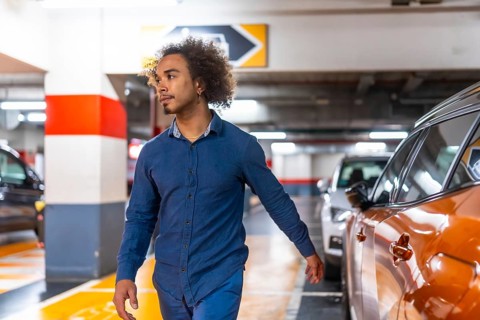 Young man with afro hair walks through a brightly lit underground parking garage, glancing right as