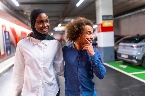 Diverse young couple happily walking arm in arm through a modern underground parking garage,