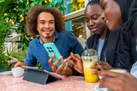 Young diverse friends in a cozy cafe sharing smartphone content, chatting and laughing over coffee