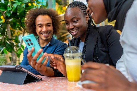 Diverse friends are happily socializing at a cafe, using a smartphone to view and share content,