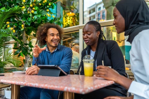 Diverse young professionals and friends gathered in a relaxed cafe, laughing, sharing ideas and