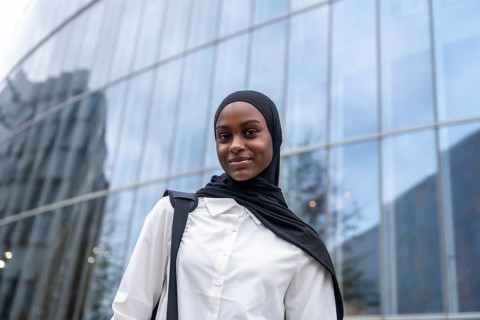 African american woman student wearing a black hijab and white shirt, carrying a backpack, standing