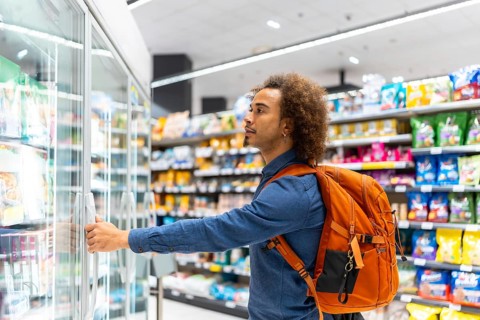 Young african american man with curly hair and a backpack opening a supermarket freezer,
