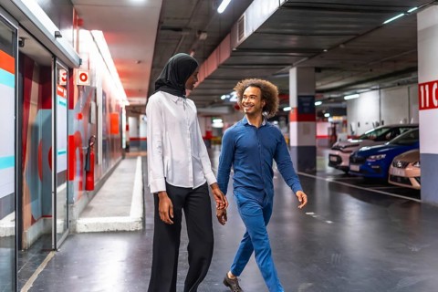 Diverse young couple walking hand in hand through an underground parking garage, sharing a loving