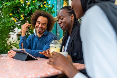 Cheerful diverse friends sitting at a cafe table, laughing and discussing content on a digital