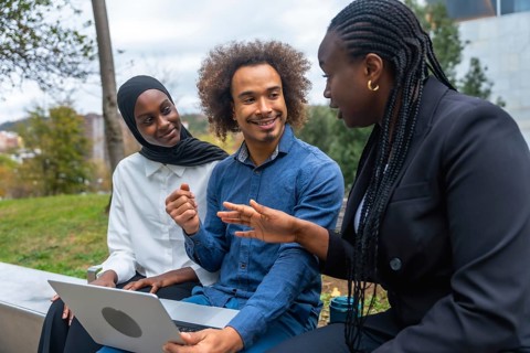 Diverse colleagues discussing and brainstorming ideas while working on a laptop together,