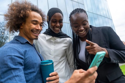 Group of diverse friends standing close together, smiling and laughing while looking at a