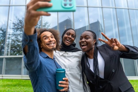 Three diverse friends smiling and laughing while taking a group selfie with a smartphone,