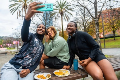 Diverse group of young adult friends smiling while taking a cheerful selfie and eating take out