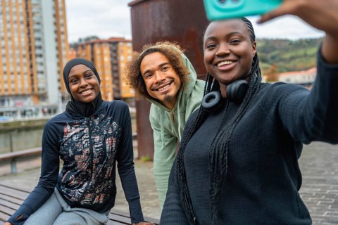 Three smiling diverse young adults enjoying friendship and making a selfie outdoors in an urban