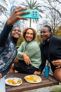 Diverse group of young adult friends smiling and laughing, holding a phone to take a selfie while
