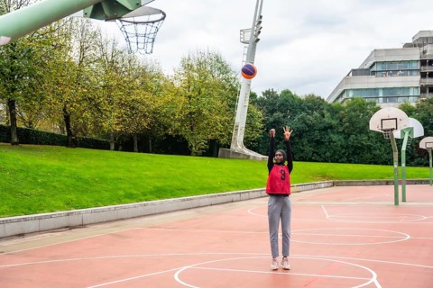 Muslim woman wearing a hijab and sportswear on an urban basketball court shooting a colorful ball,