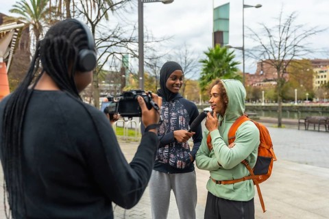 Journalist filming and interviewing a diverse group of young adults in an urban park, capturing